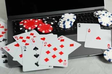 Photo of Online poker. Playing cards, chips and laptop on light grey table