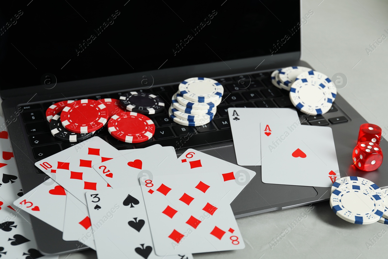 Photo of Online poker. Playing cards, chips, dice and laptop on light grey table