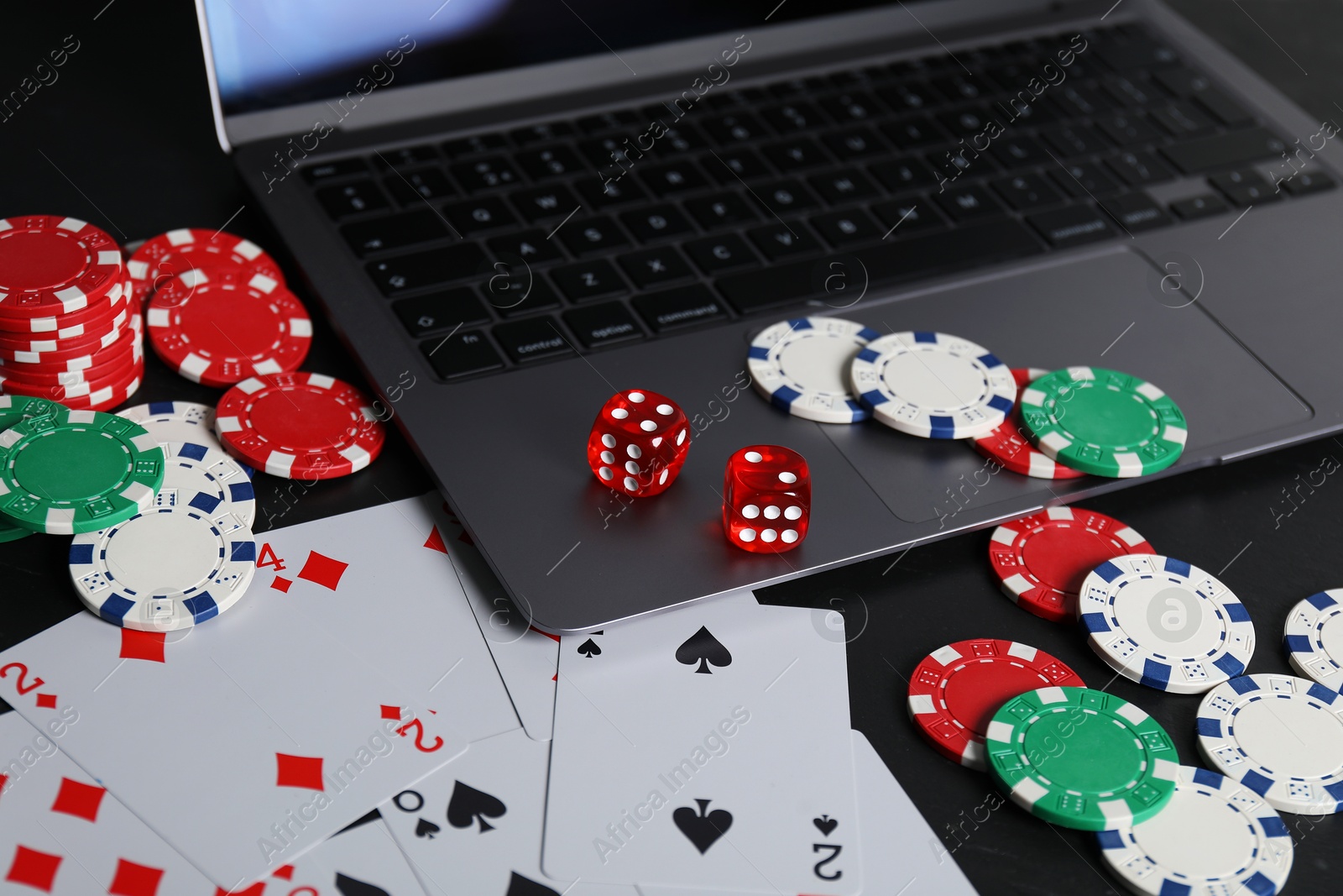 Photo of Online poker. Playing cards, chips, dice and laptop on black table, closeup