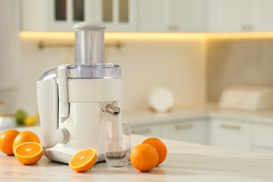 Photo of Modern juicer, oranges and glass on white marble table in kitchen, space for text