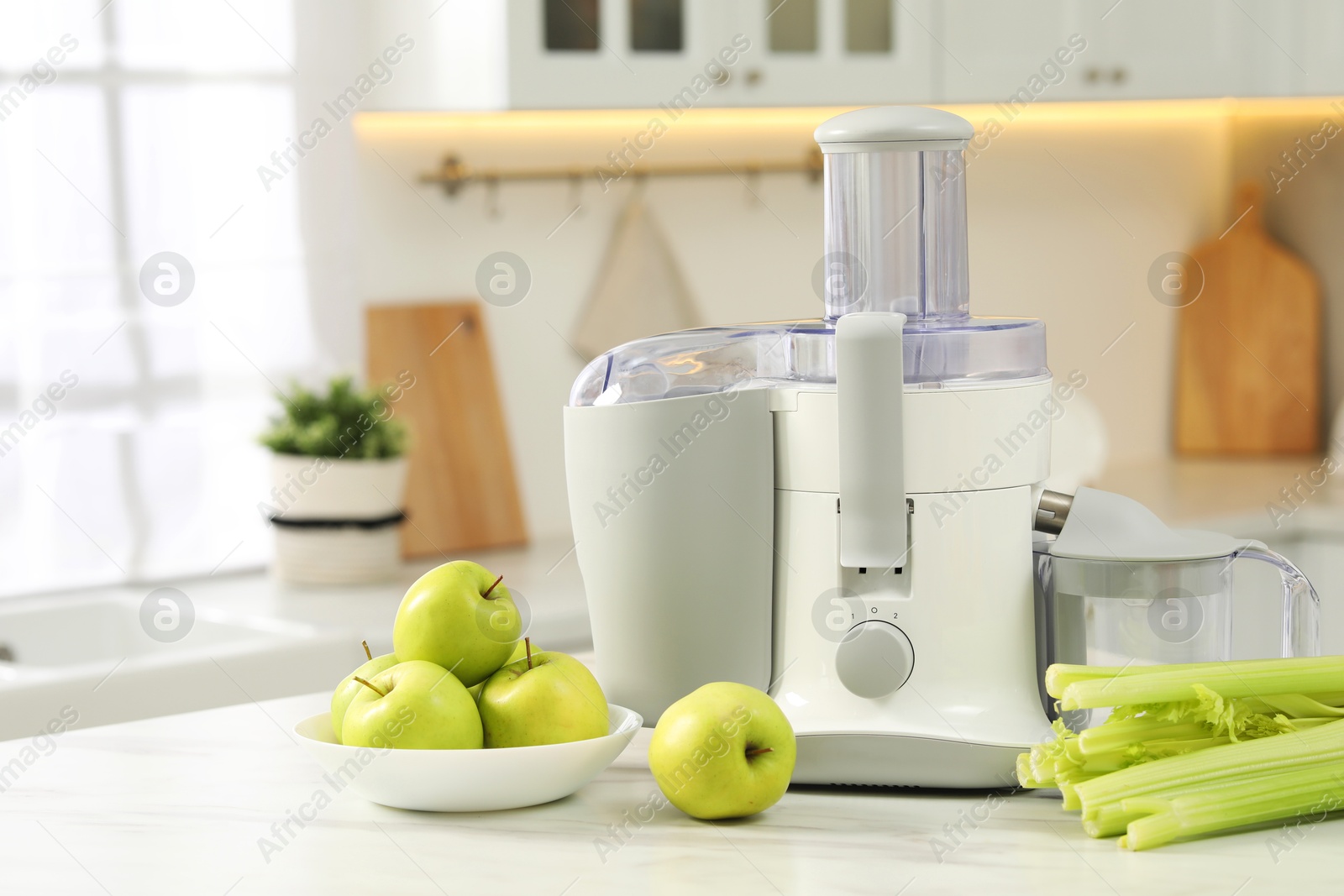 Photo of Modern juicer, celery and apples on white marble table in kitchen