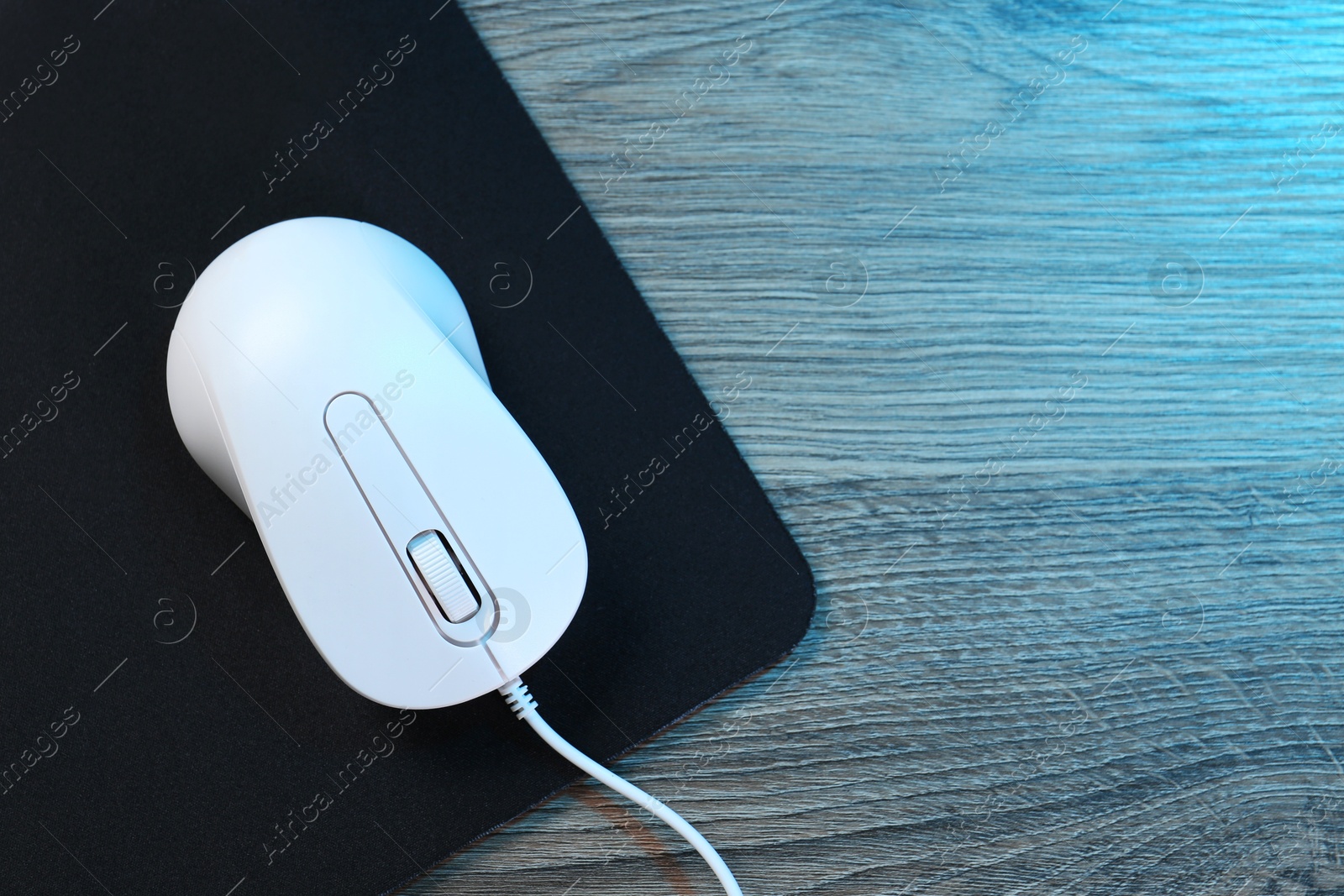 Photo of Computer mouse with mousepad on wooden table, top view. Space for text