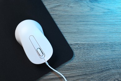 Photo of Computer mouse with mousepad on wooden table, top view. Space for text