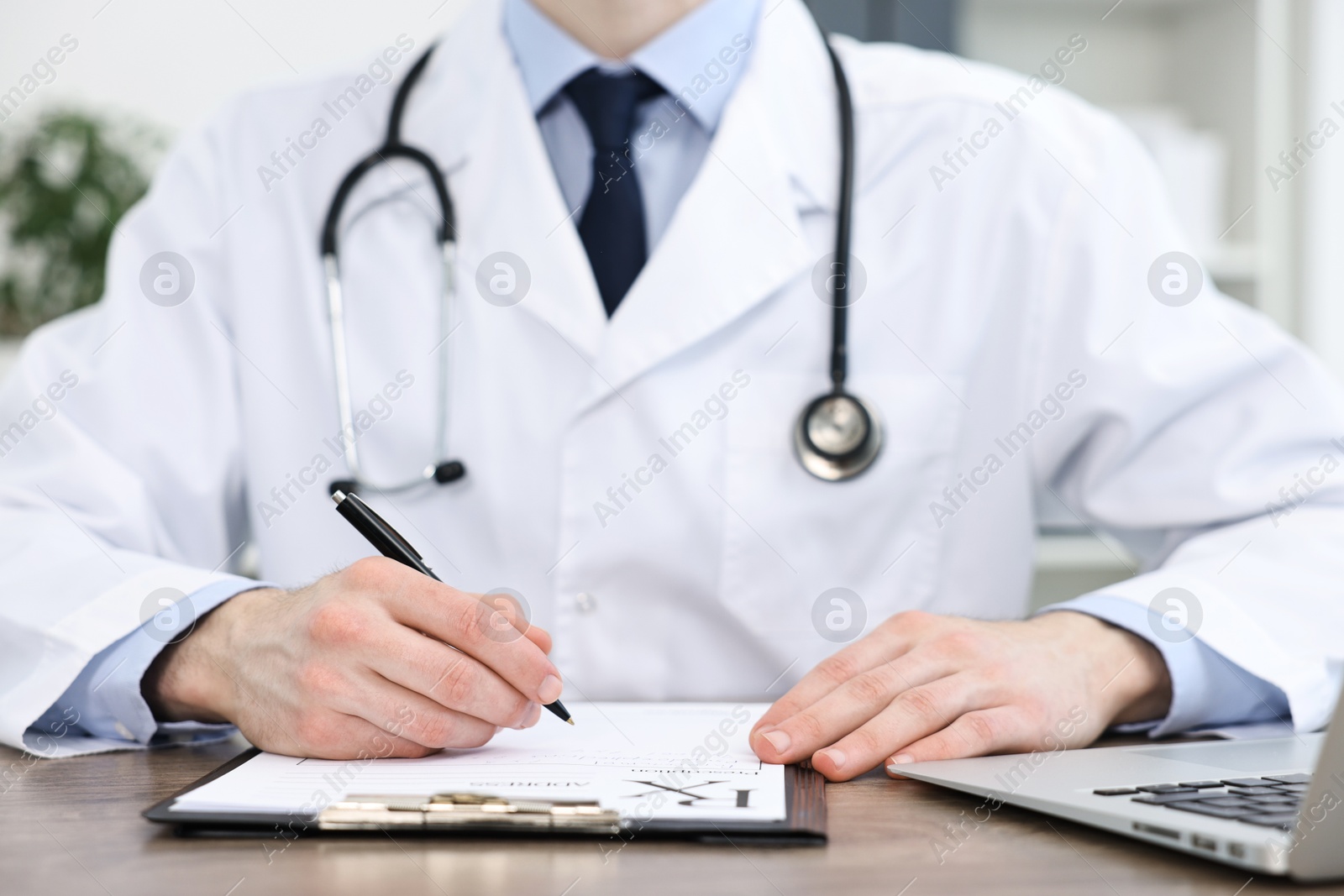 Photo of Doctor writing prescription at wooden table in clinic, closeup