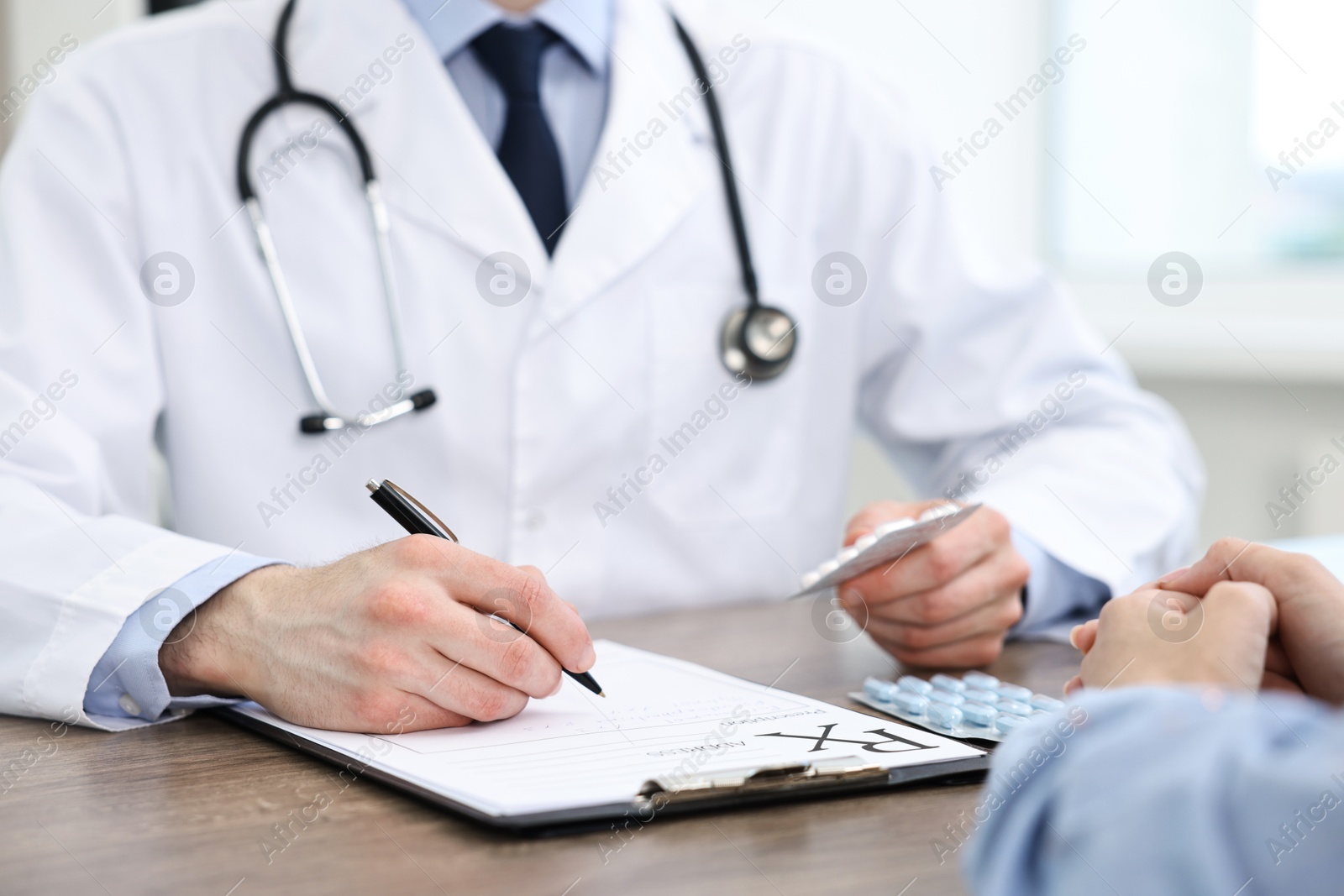 Photo of Doctor with pills writing prescription for patient at wooden table in clinic, closeup