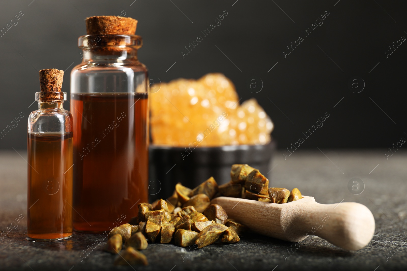 Photo of Honey tincture and scoop with propolis granules on grey textured table, closeup. Alternative medicine