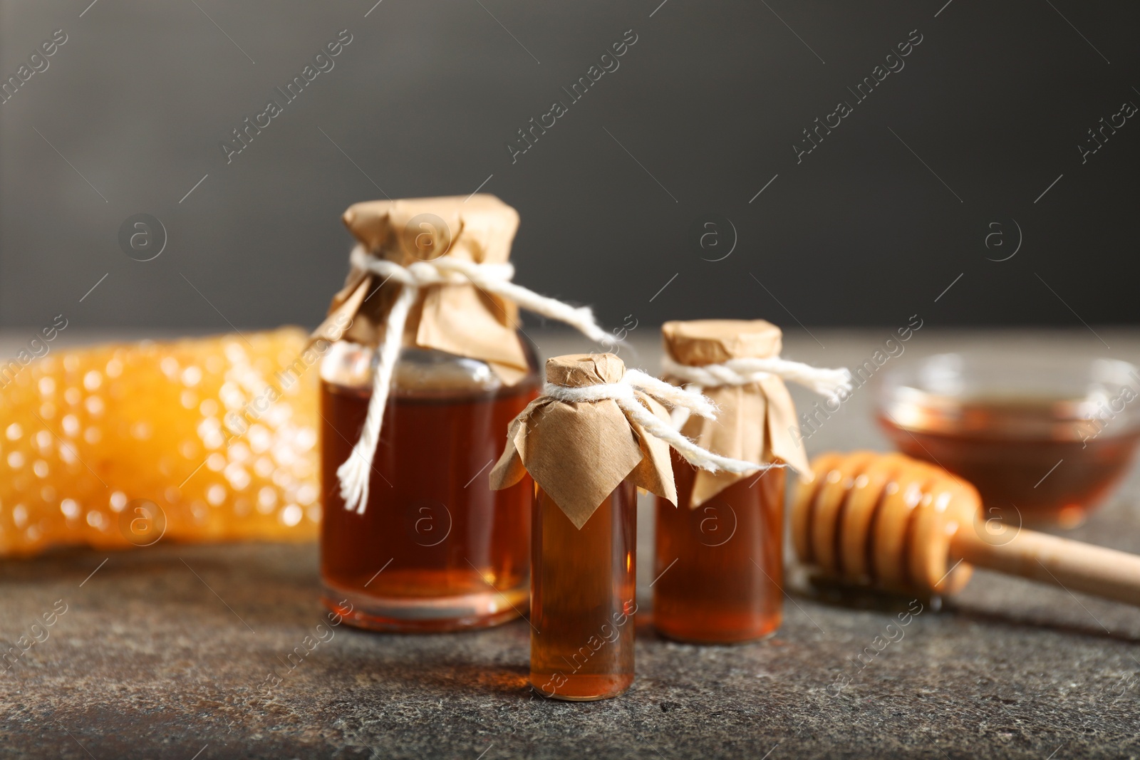 Photo of Honey tinctures, dipper and honeycomb on grey textured table, closeup. Alternative medicine