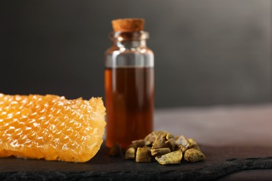 Photo of Honey tincture, honeycomb and pile of propolis granules on table, closeup. Alternative medicine