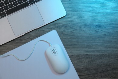 Photo of Computer mouse with mousepad and laptop on wooden table, flat lay. Space for text