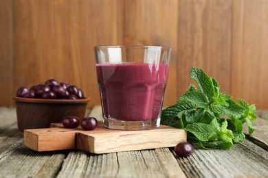 Photo of Tasty fresh acai juice in glass with berries and mint on wooden table