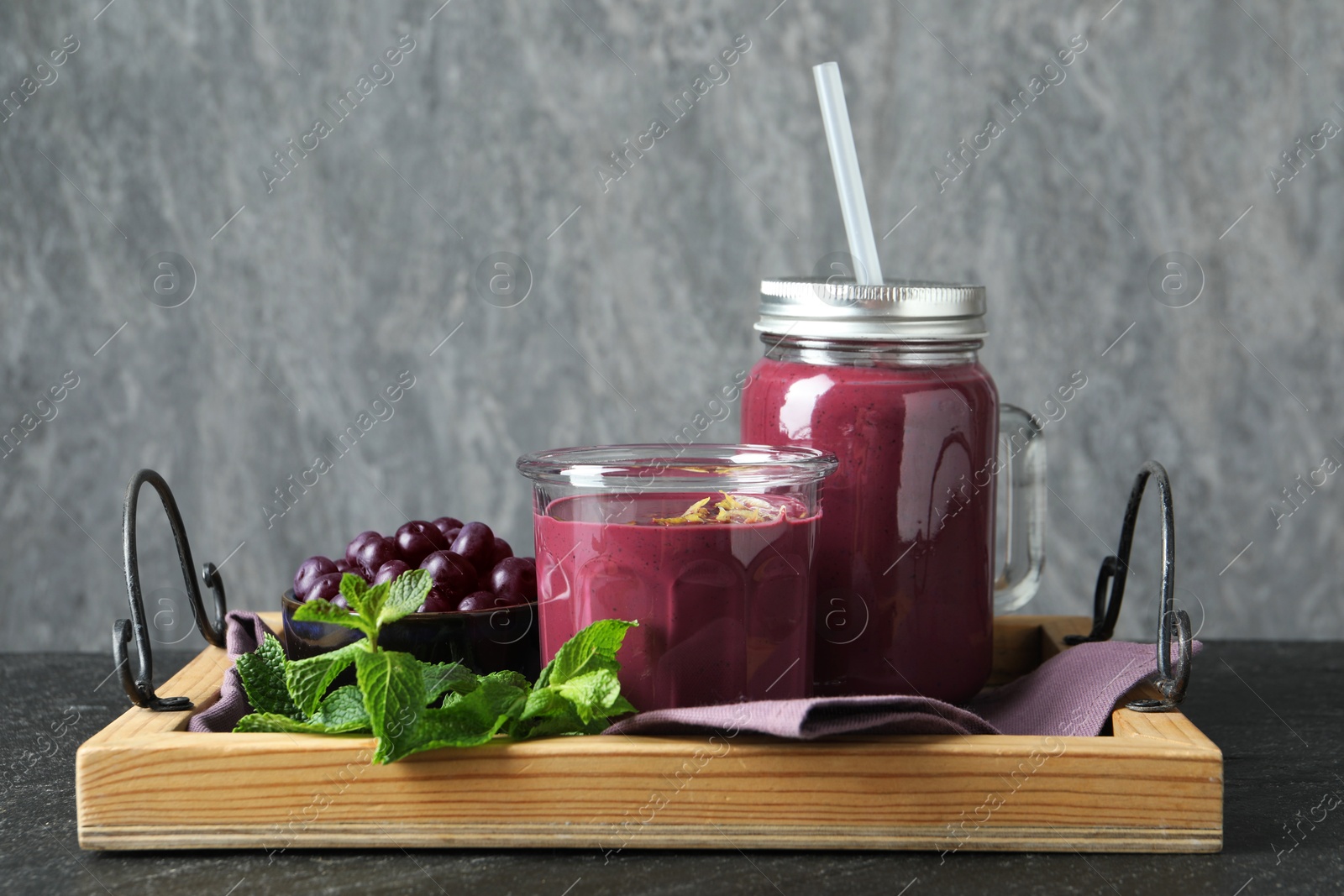 Photo of Tasty fresh acai juice with mint and berries on grey table