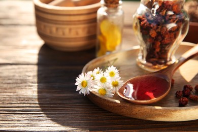 Photo of Tincture in spoon, chamomiles and dried berries on wooden table