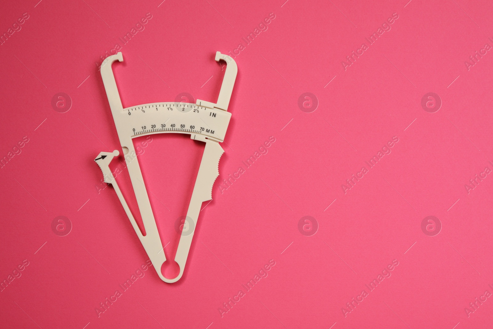 Photo of Plastic body fat caliper on pink background, top view. Space for text