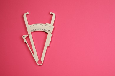 Photo of Plastic body fat caliper on pink background, top view. Space for text