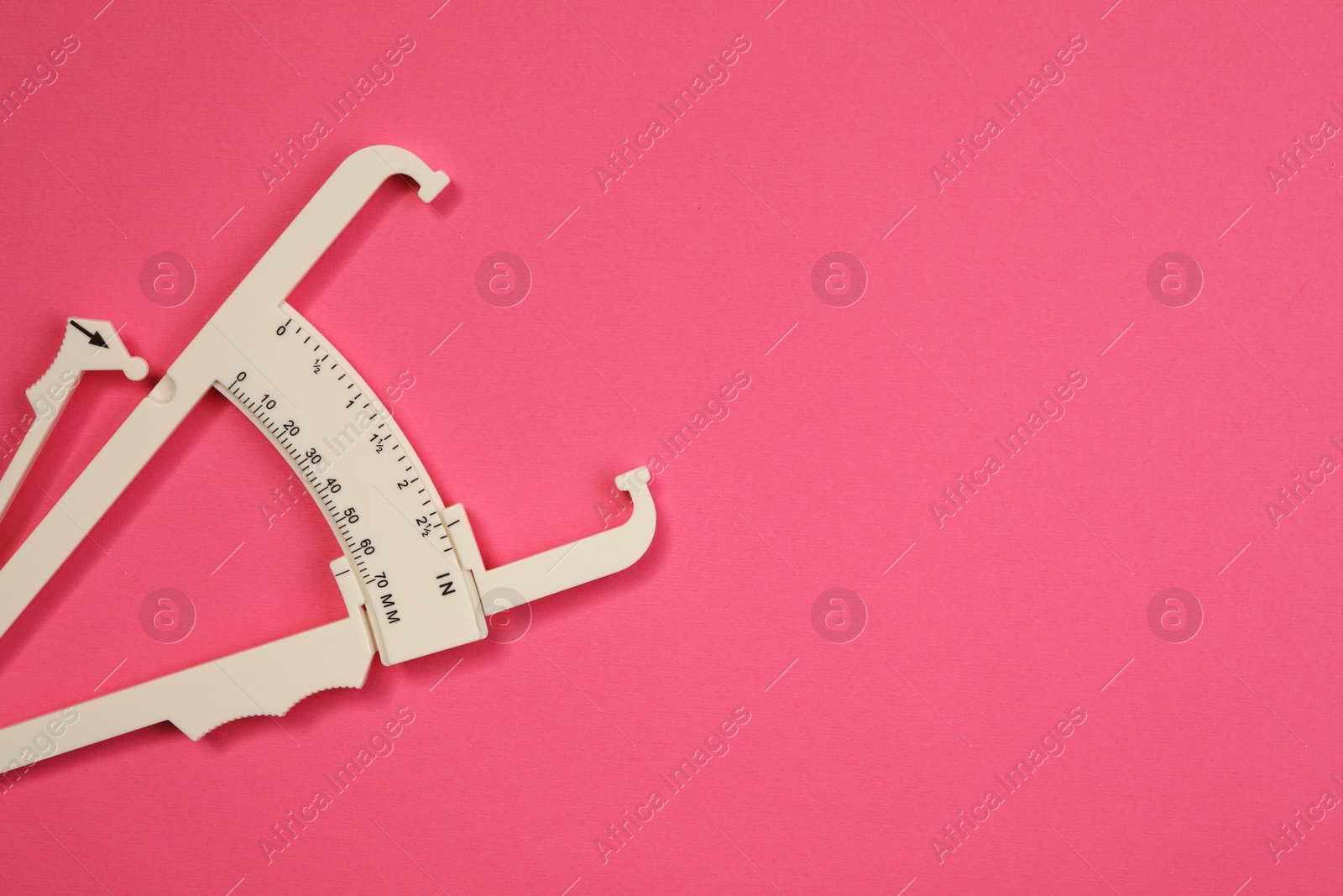 Photo of Plastic body fat caliper on pink background, top view. Space for text