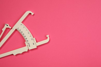 Photo of Plastic body fat caliper on pink background, top view. Space for text