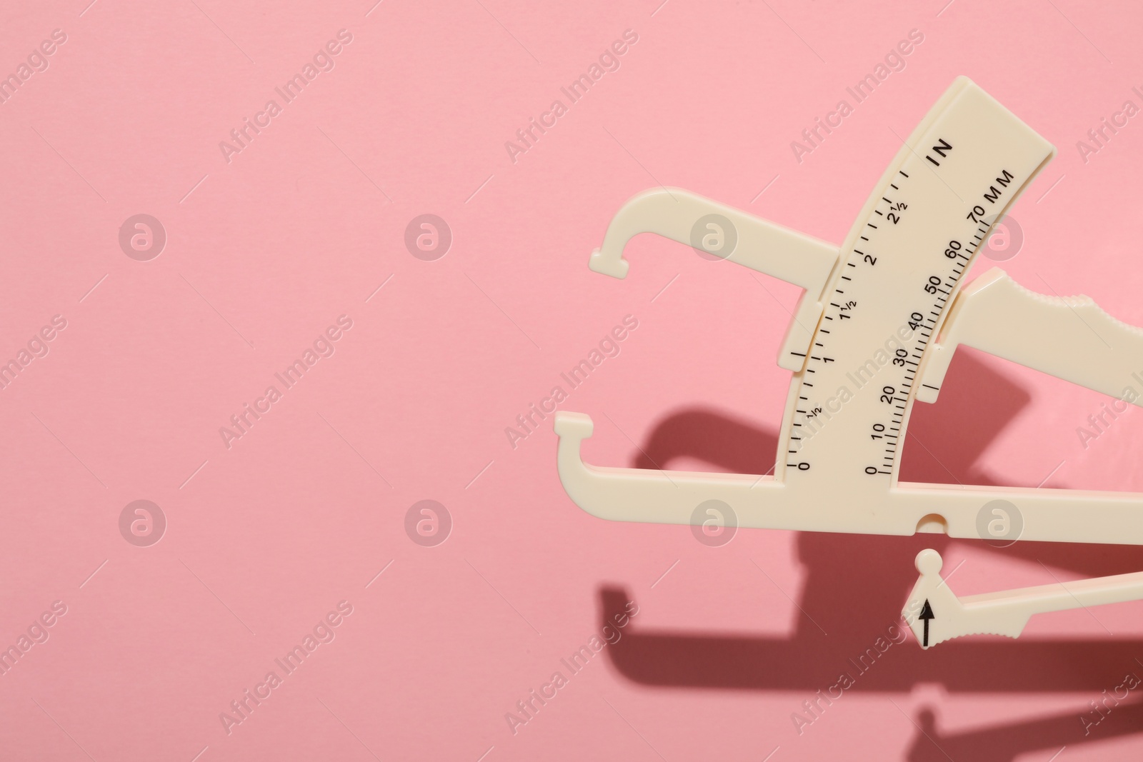 Photo of Plastic body fat caliper on pink background. Space for text