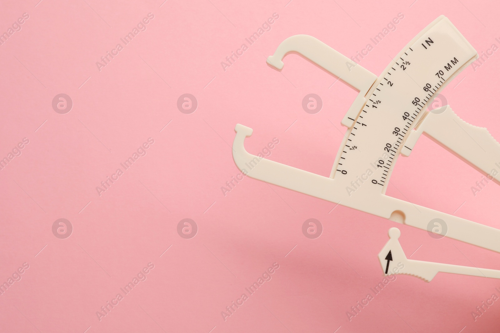 Photo of Plastic body fat caliper on pink background, closeup. Space for text