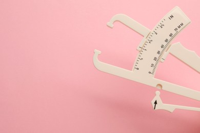 Photo of Plastic body fat caliper on pink background, closeup. Space for text