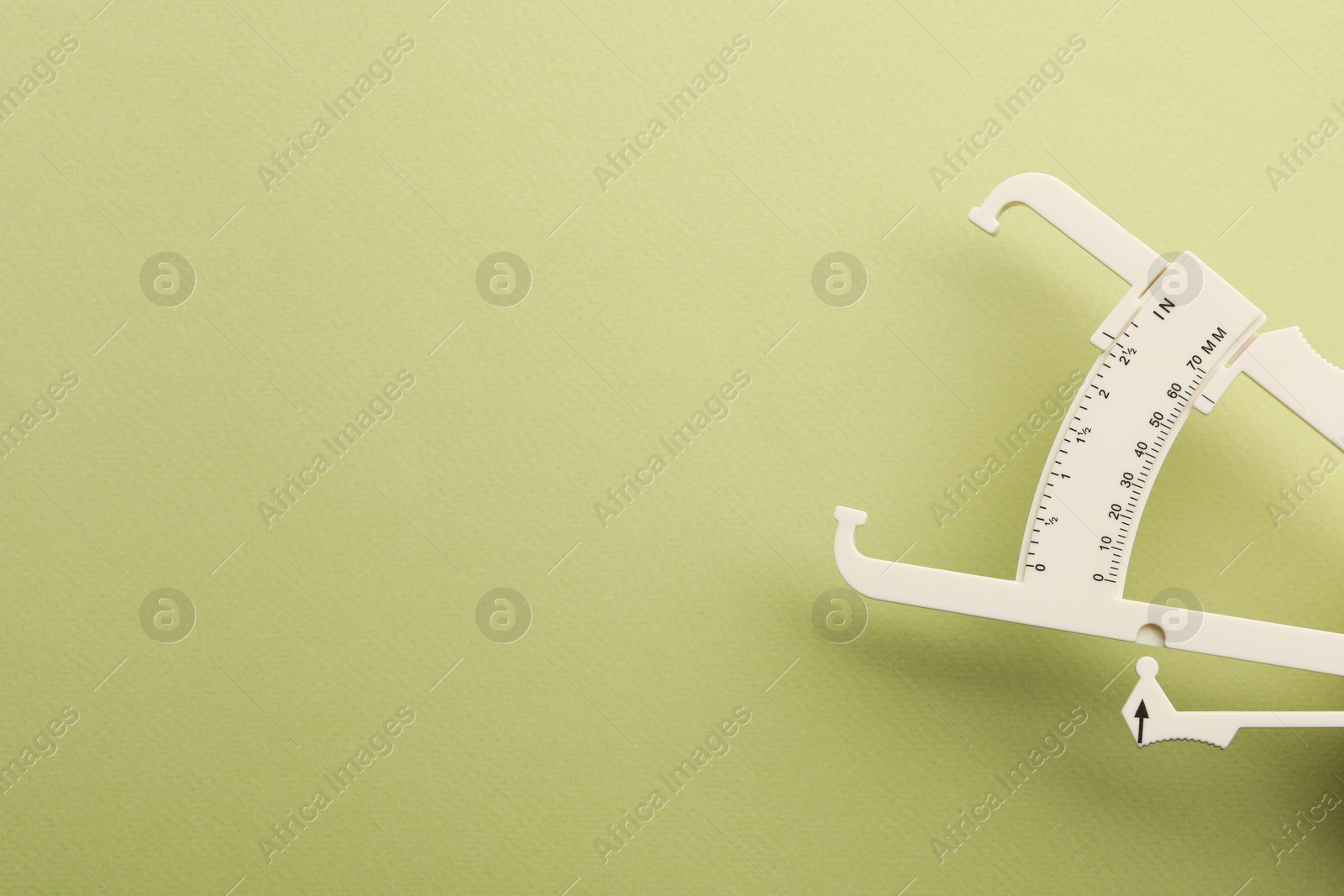 Photo of Plastic body fat caliper on light green background. Space for text