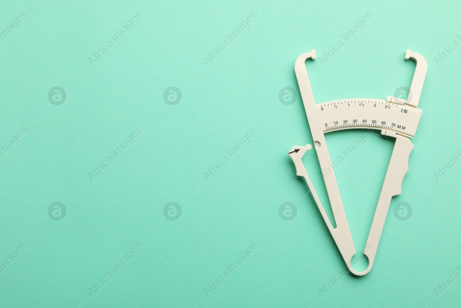 Photo of Plastic body fat caliper on turquoise background, top view. Space for text