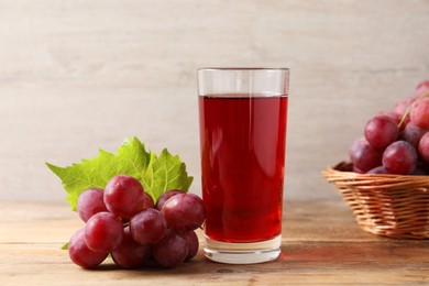 Photo of Tasty juice in glass, fresh grapes and leaf on wooden table