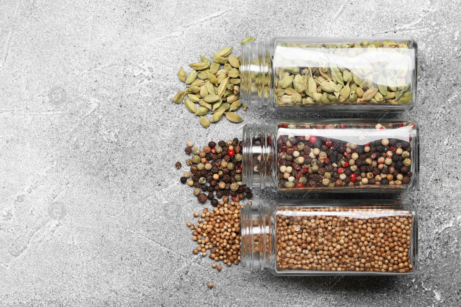 Photo of Different spices in glass jars on grey table, top view. Space for text