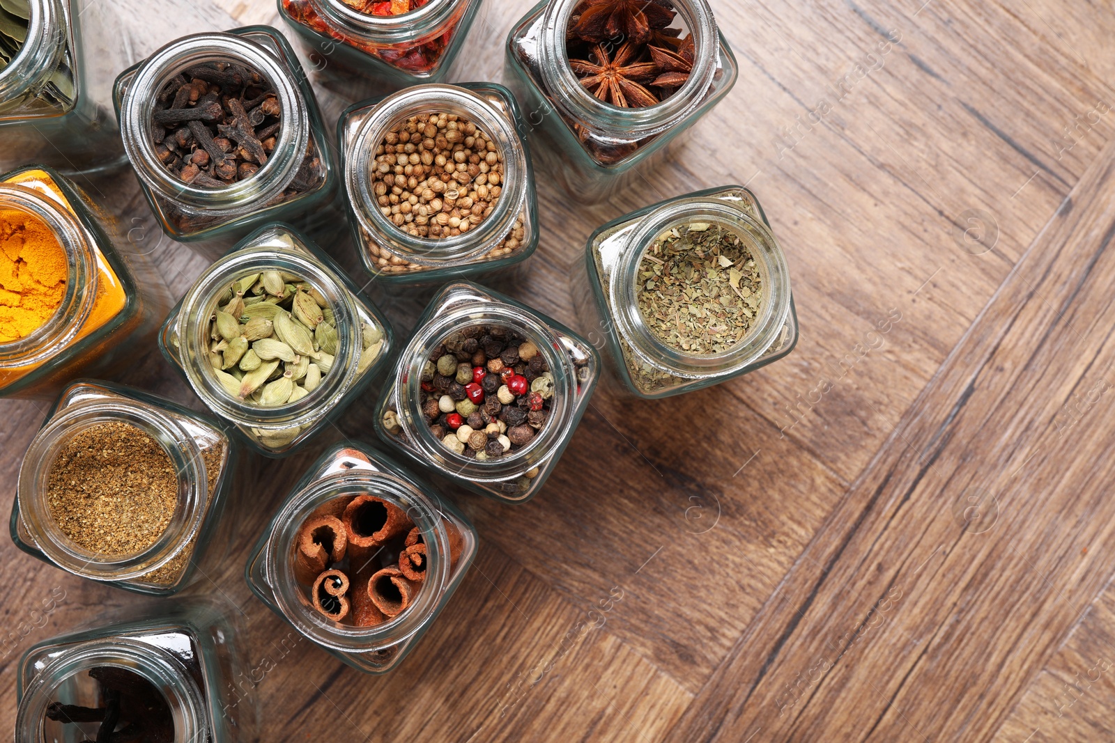 Photo of Different spices in glass jars on wooden table, flat lay. Space for text