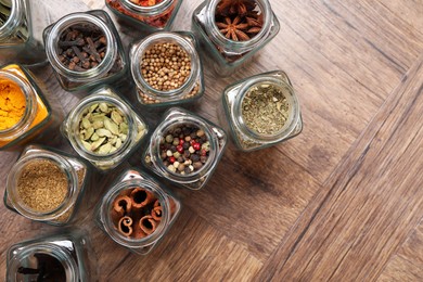 Photo of Different spices in glass jars on wooden table, flat lay. Space for text