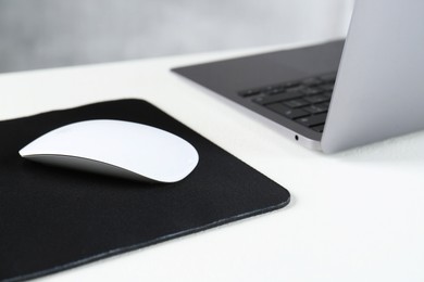 Photo of Computer mouse with mousepad and laptop on white table, closeup