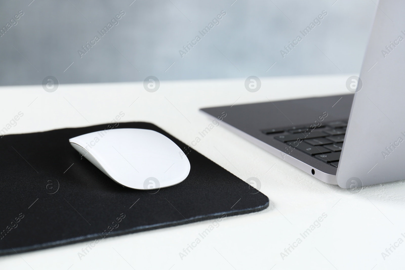 Photo of Computer mouse with mousepad and laptop on white table, closeup