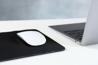 Photo of Computer mouse with mousepad and laptop on white table, closeup