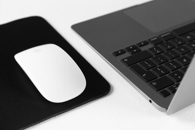 Photo of Computer mouse with mousepad and laptop on white table, closeup