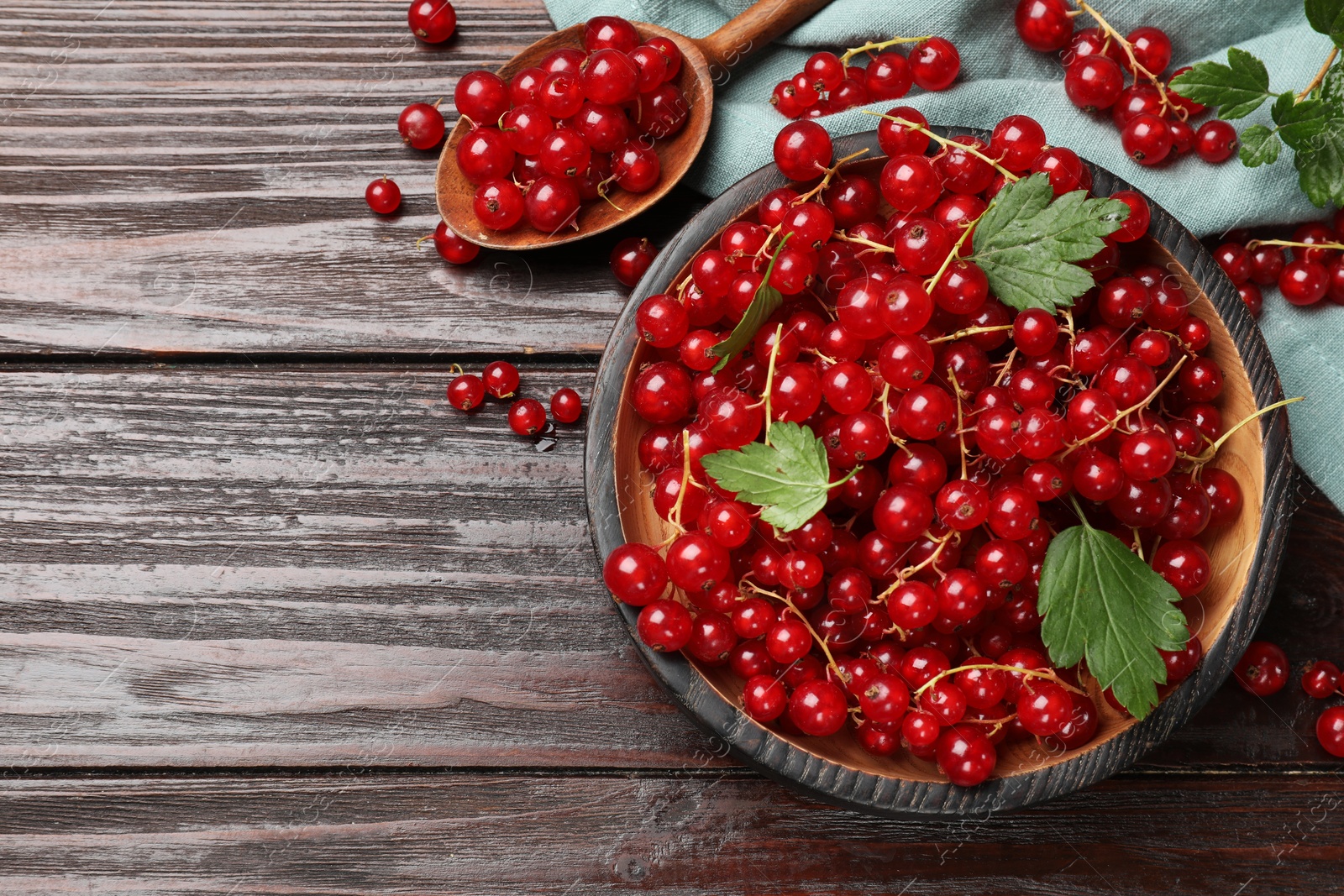 Photo of Fresh red currants and green leaves on wooden table, flat lay. Space for text