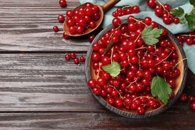 Photo of Fresh red currants and green leaves on wooden table, flat lay. Space for text