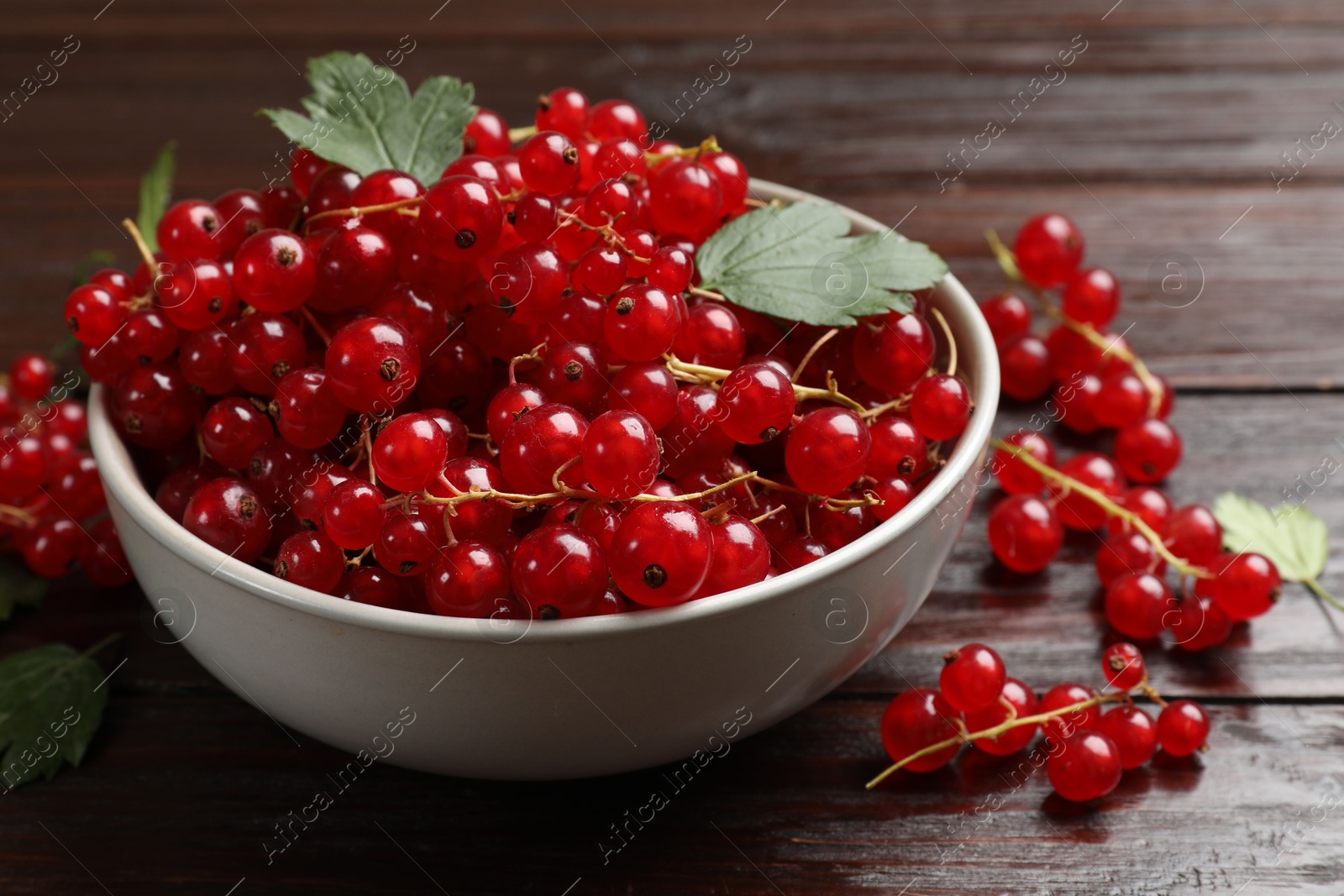 Photo of Fresh red currants in bowl on wooden table, closeup