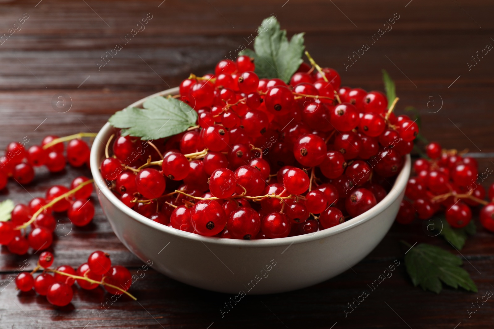 Photo of Fresh red currants in bowl on wooden table, closeup