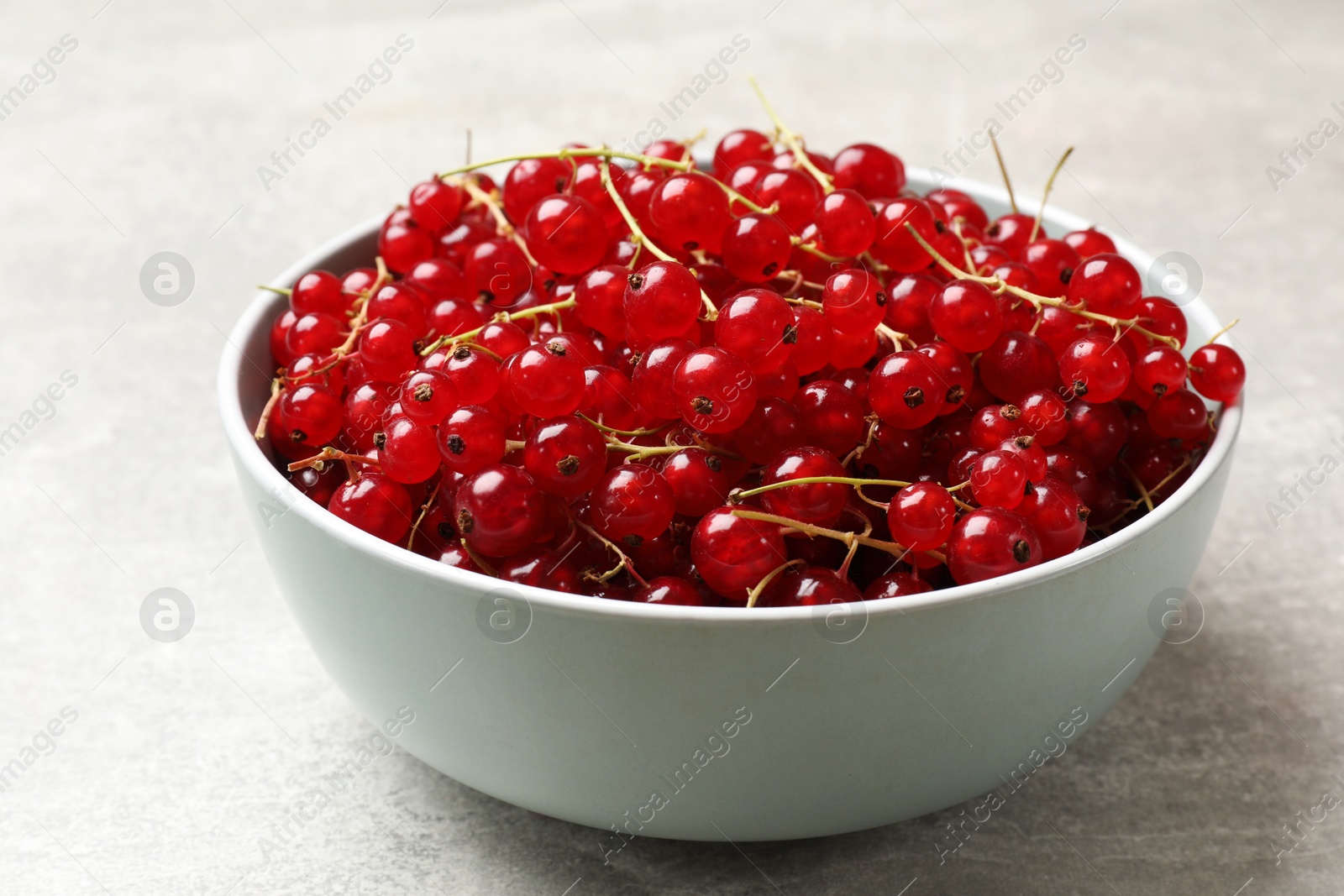 Photo of Fresh red currants in bowl on light grey table, closeup