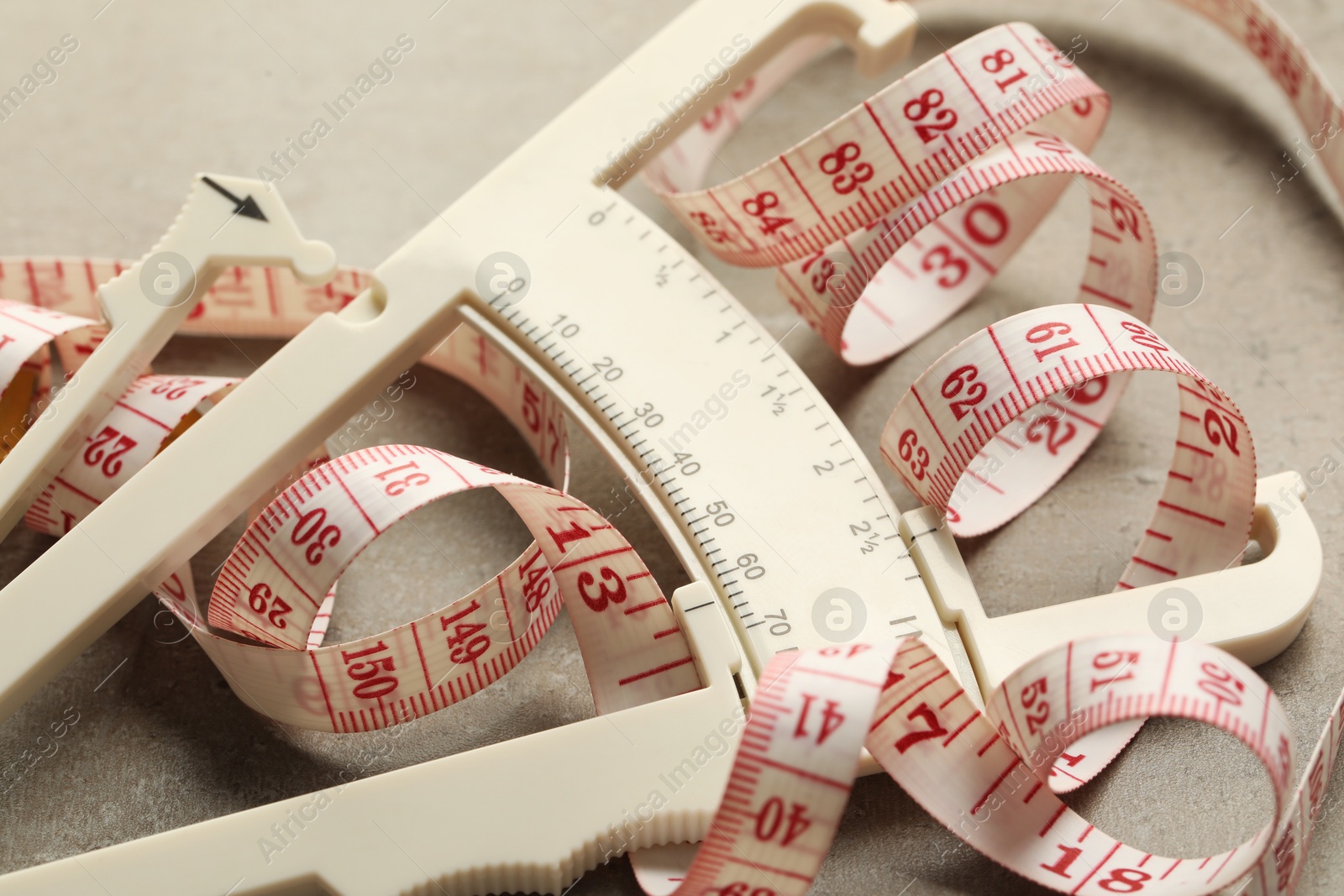 Photo of Plastic body fat caliper and measuring tape on grey table, closeup