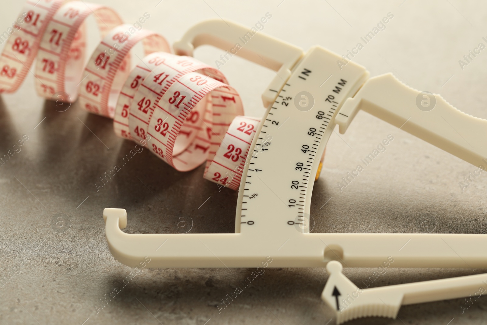 Photo of Plastic body fat caliper and measuring tape on grey table, closeup