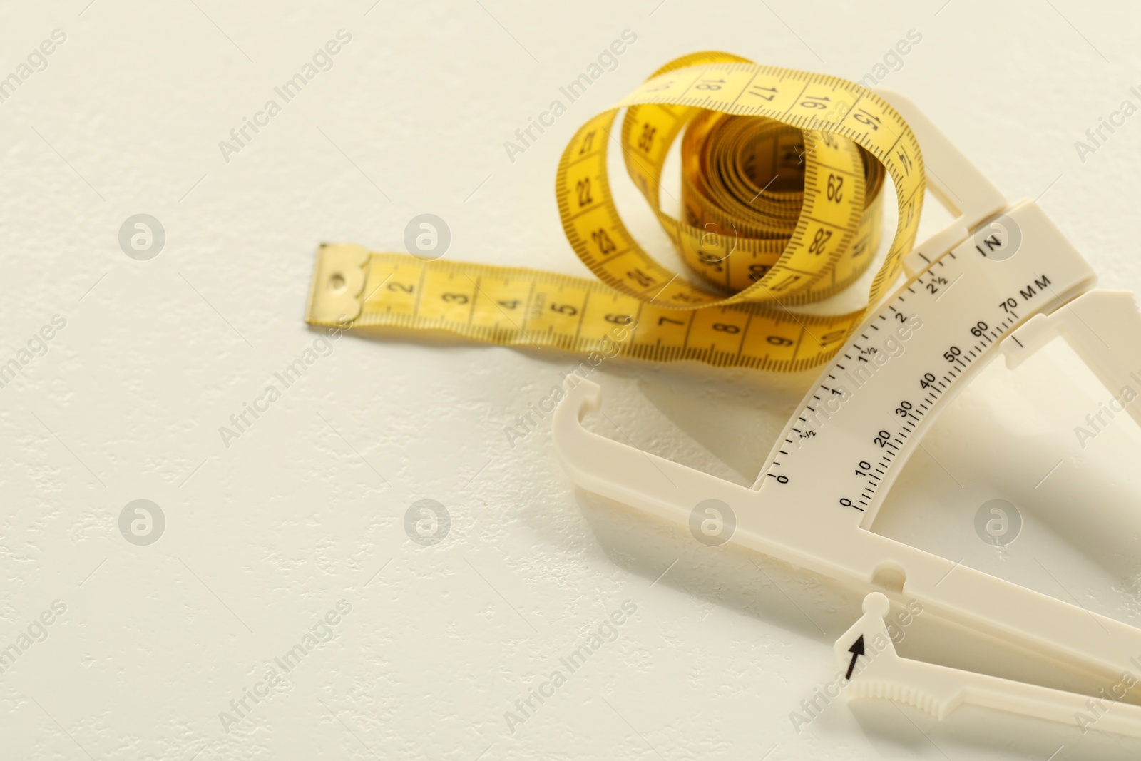 Photo of Plastic body fat caliper and measuring tape on white table, closeup. Space for text