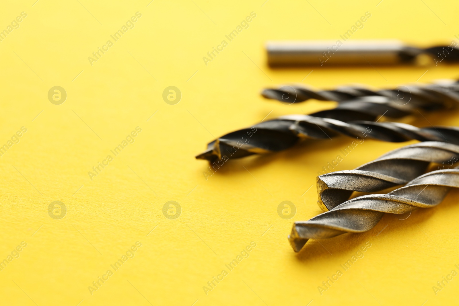 Photo of Many different drill bits on yellow background, closeup. Space for text