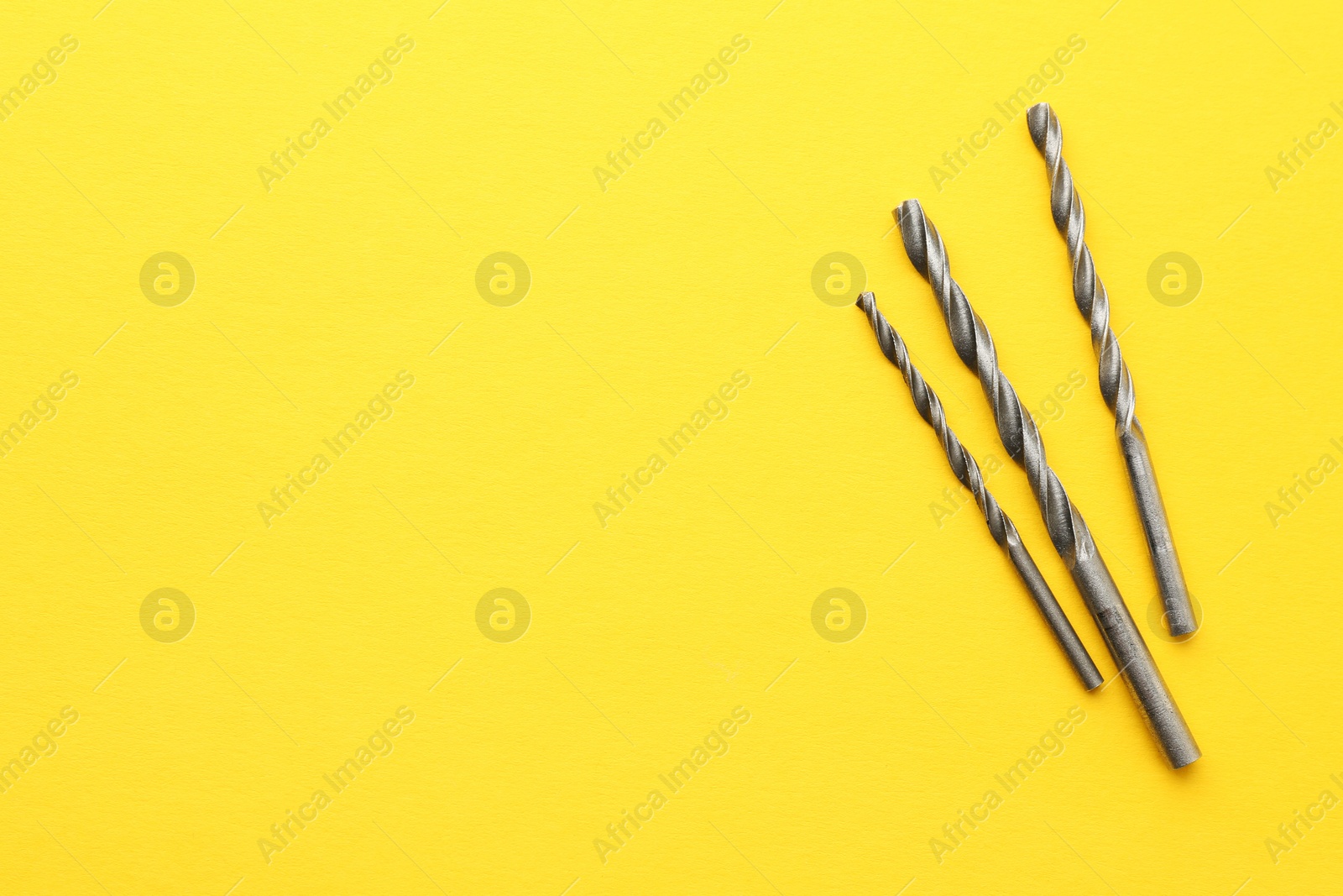 Photo of Different drill bits on yellow background, top view. Space for text