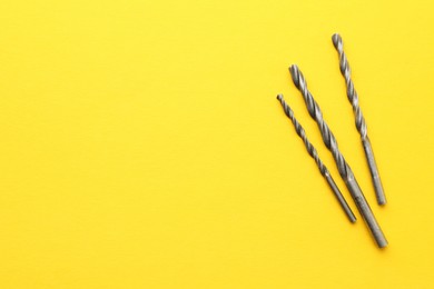 Photo of Different drill bits on yellow background, top view. Space for text