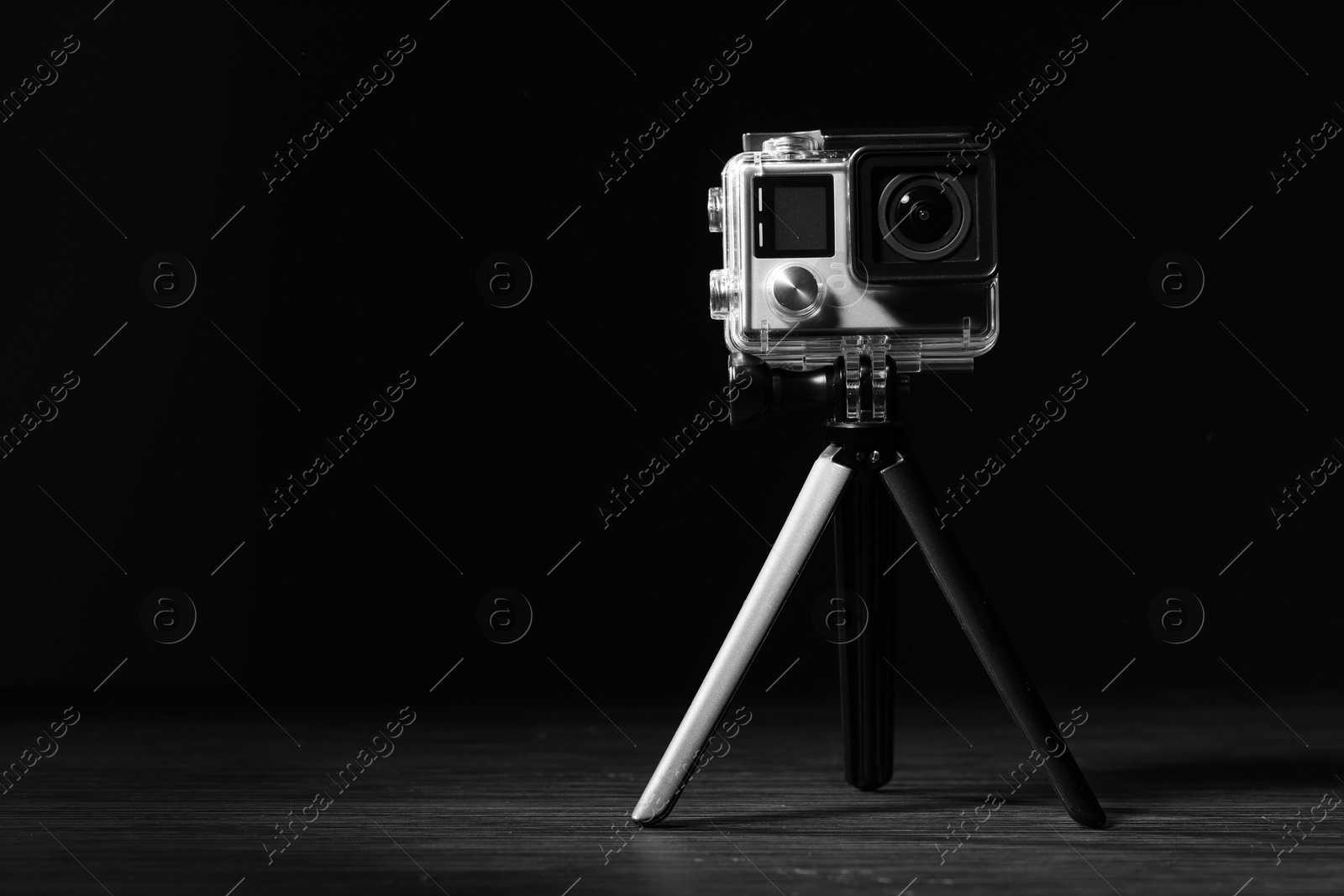 Photo of Modern action camera and tripod on wooden surface against black background. Space for text