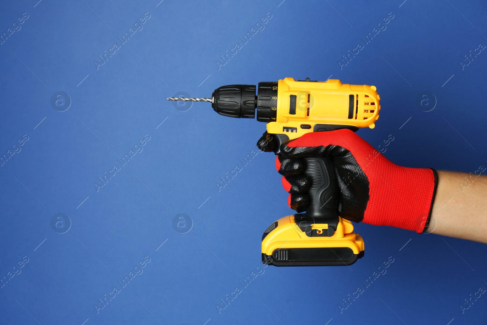 Photo of Man with cordless electric drill on blue background, closeup. Space for text