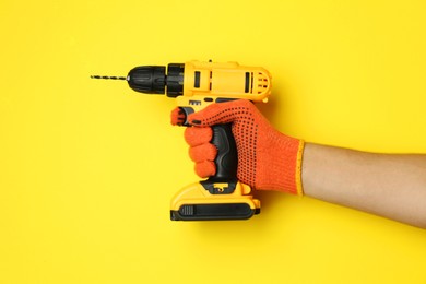 Photo of Man with cordless electric drill on yellow background, closeup