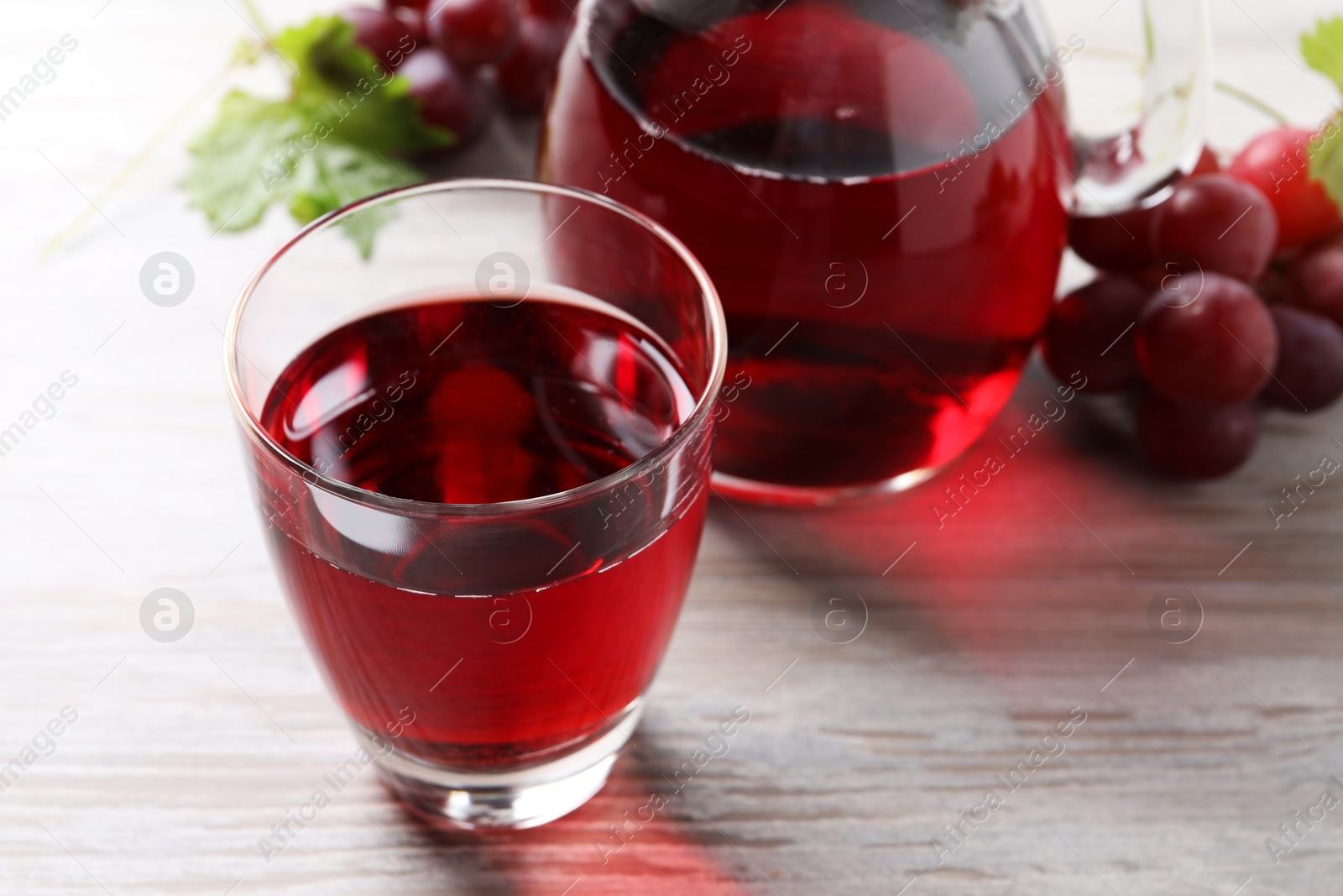 Photo of Tasty grape juice and berries on light wooden table, closeup