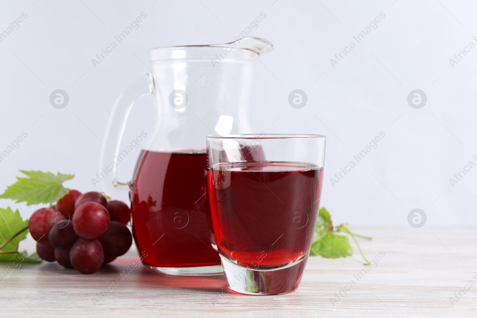 Photo of Tasty grape juice, leaves and berries on light wooden table