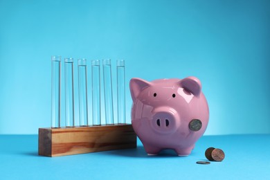 Photo of Water save concept. Piggy bank, coins and liquid in test tubes on light blue background